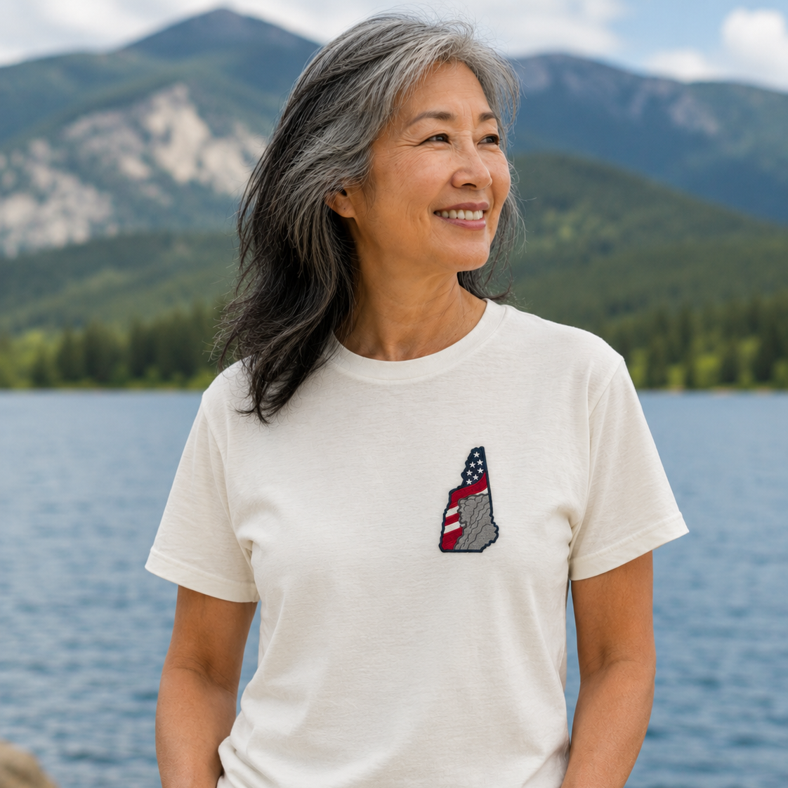 Woman wearing a white t-shirt with a graphic design by a lake and mountains
