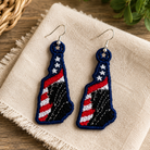 Pair of blue earrings with American flag design on a beige cloth with green leaves in the background