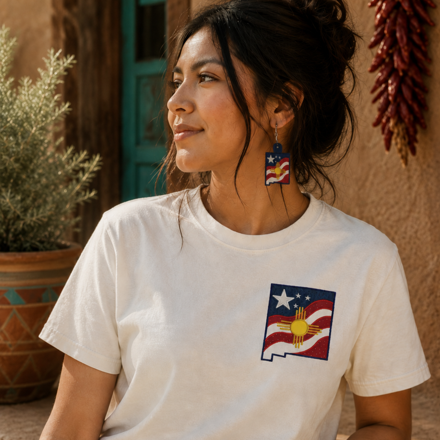 Woman wearing a white t-shirt with a graphic design, sitting outdoors against a rustic wall.