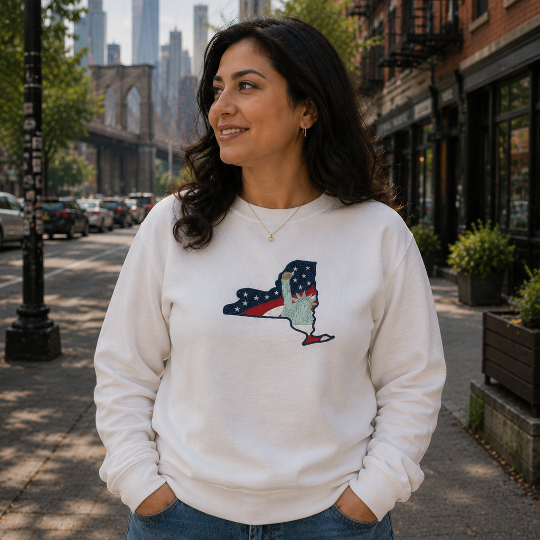 Woman wearing a white sweatshirt with a graphic design, standing on a city street with a skyline in the background.
