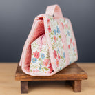 A pink floral fabric organizer bag with a matching zippered pouch, displayed on a small wooden stand against a dark gray background.