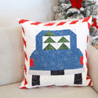 Decorative pillow with a Christmas truck design on a couch next to a decorated tree.