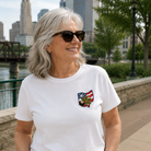 Woman wearing a white t-shirt with a pocket design, standing outdoors with a cityscape in the background.