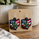 Pair of earrings on a card with a plant and container in the background