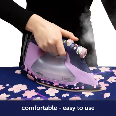 Person using a purple and gray iron on a floral ironing board with 'aliso' branding.