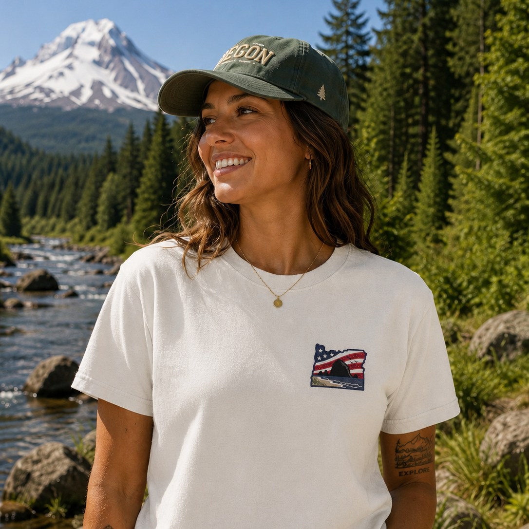Person wearing a cap and t-shirt with a nature-themed design, standing in front of a mountain and river.