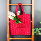 Red polka dot tote bag with white flowers on a wooden ladder against a gray wall.