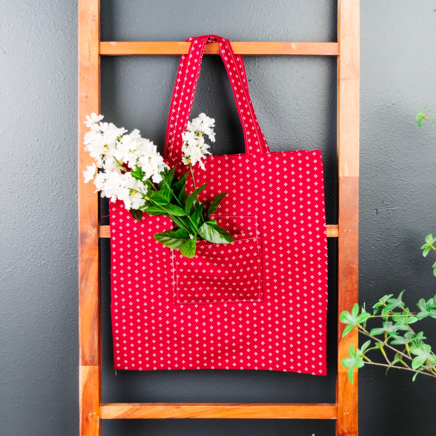 Red polka dot tote bag with white flowers on a wooden ladder against a gray wall.