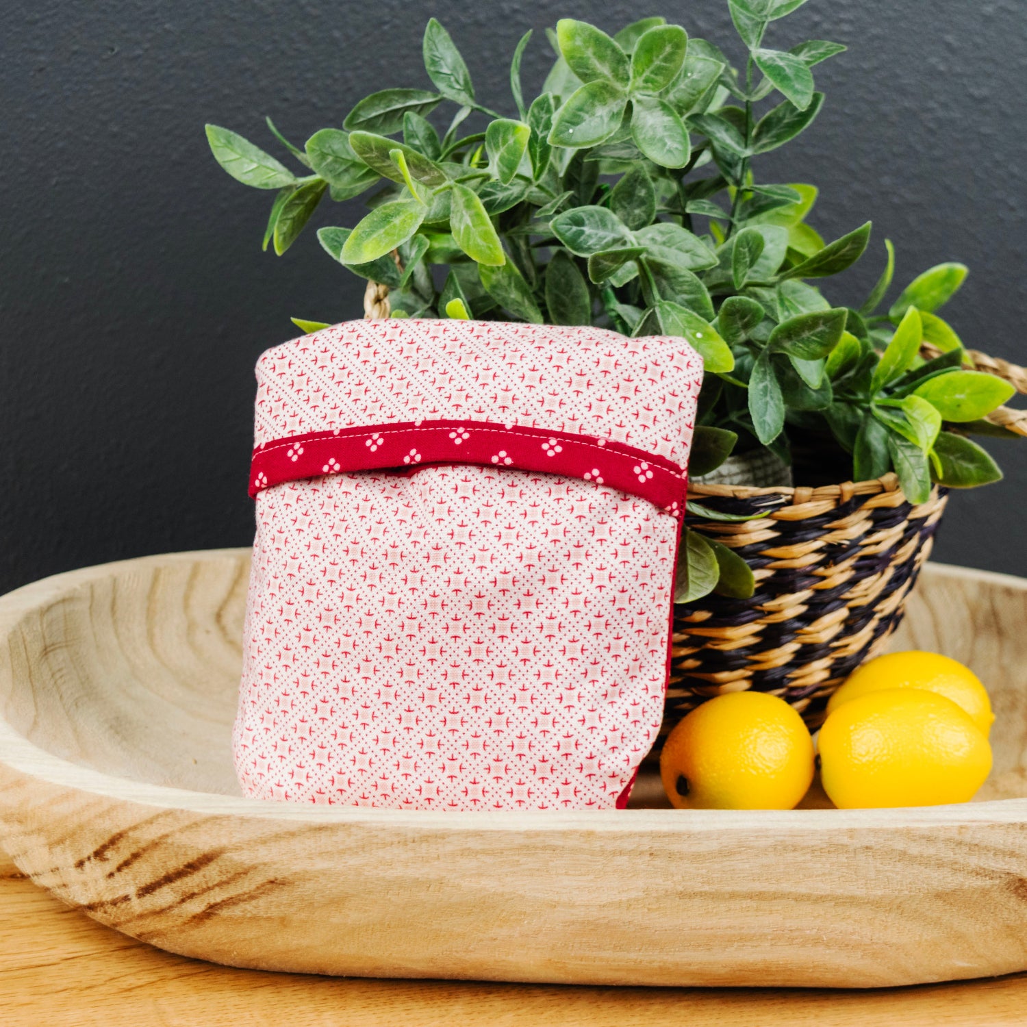 Small potted plant with a red ribbon on a wooden tray with lemons against a dark background