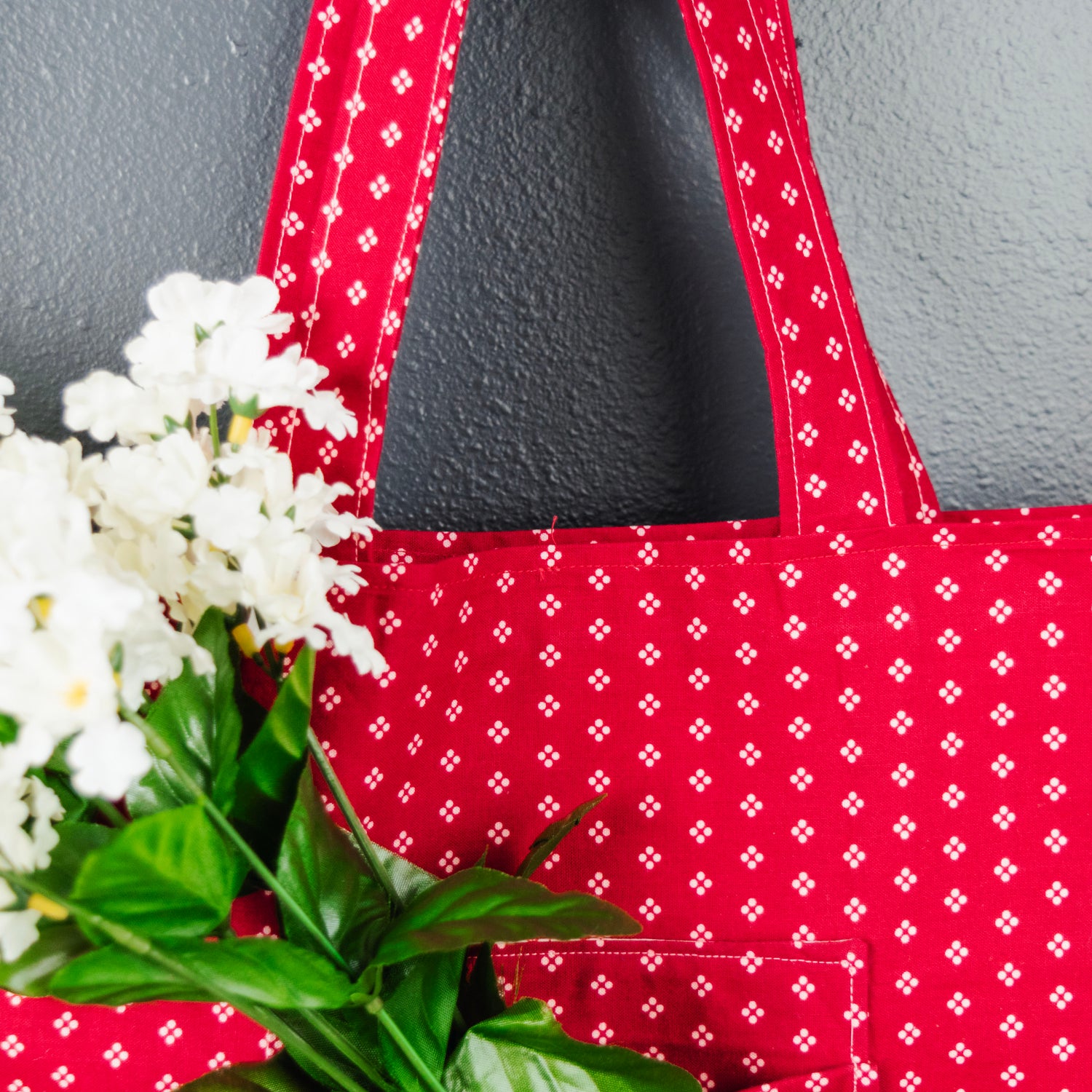 Red patterned tote bag with a bouquet of white flowers on a gray background