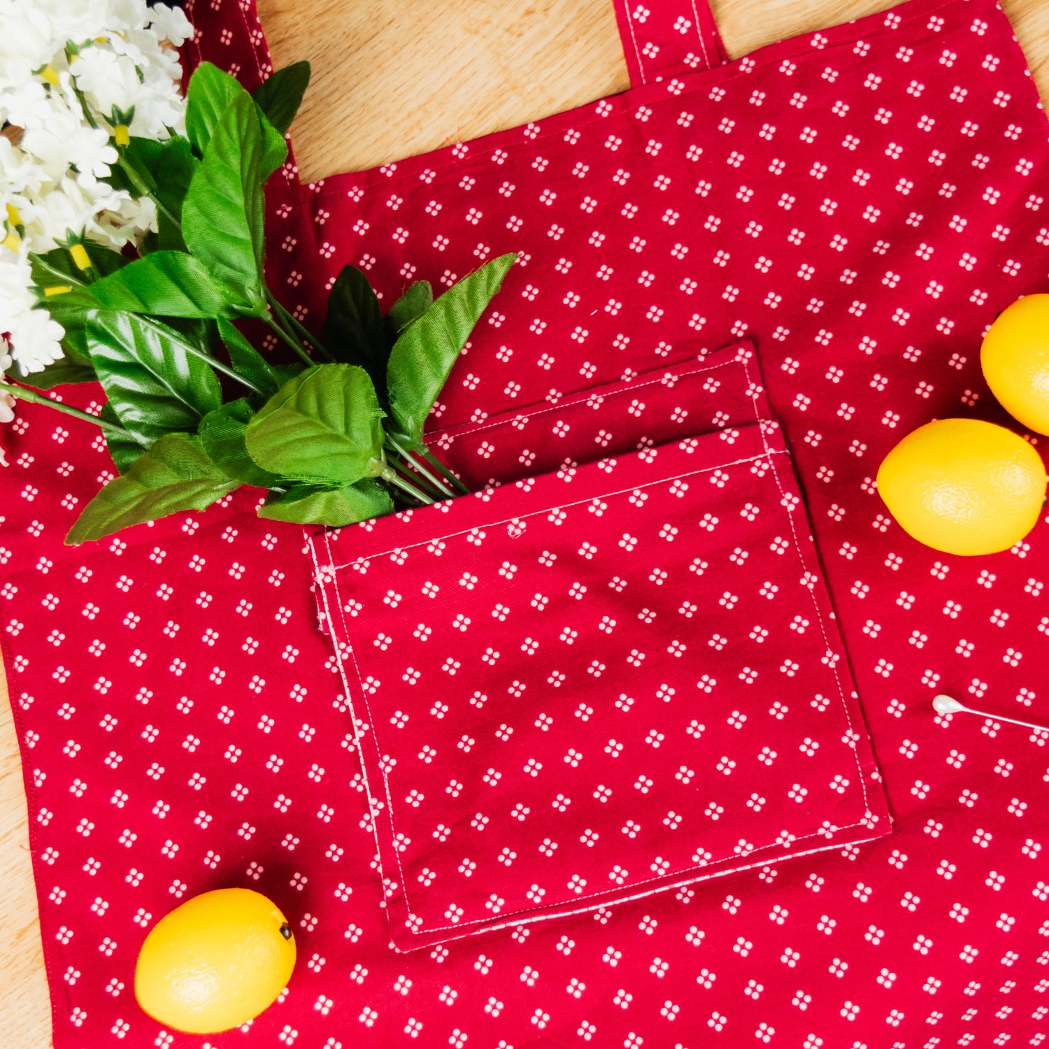 Red patterned fabric with white flowers, green leaves, and yellow fruits on a wooden surface.