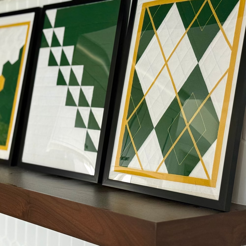 Three framed geometric art pieces on a wooden shelf.