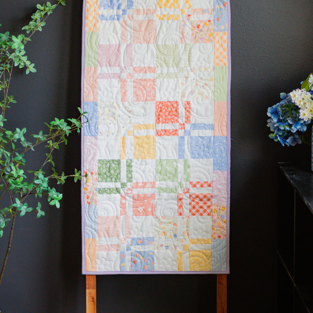 Quilt with colorful geometric pattern on a wooden hanger against a dark background