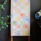 Quilt with colorful geometric pattern on a wooden hanger against a dark background