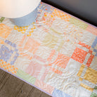 Colorful quilt with a wooden basket of Easter eggs and carrots on a table.
