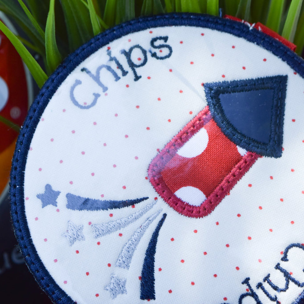 Circular patch with a red and blue design and text on a white background, placed on grass.