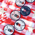 Set of round labels with various designs on a red and white checkered tablecloth.