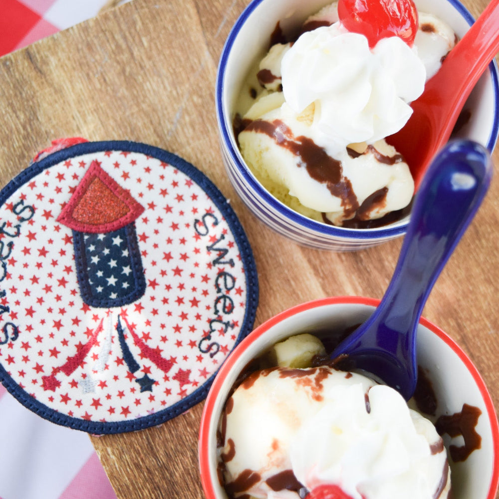 Two small bowls of ice cream with a cherry on top, served with spoons, on a wooden board with a 'Sweets' sign.