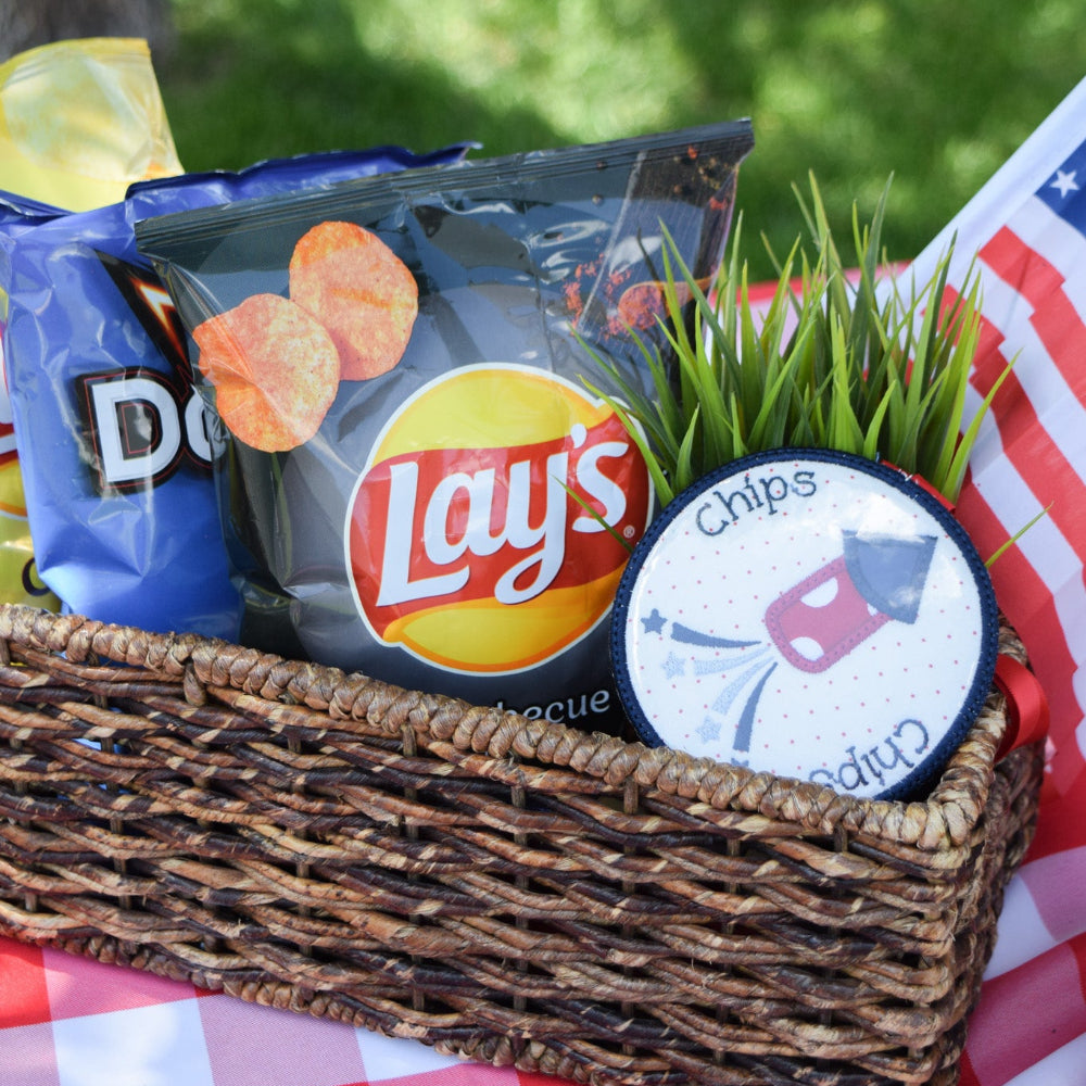 Basket with Lay's potato chips and Doritos on a checkered tablecloth outdoors