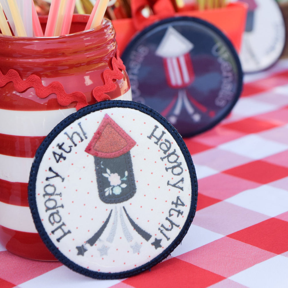 Red and white striped jar with straws and a 'Happy 4th!' label on a checkered tablecloth.