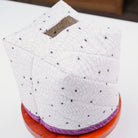 A quilted white tissue box cover with a black spiderweb pattern and small black spider motifs, displayed on a wooden stand on a white table.