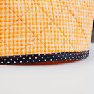 Close-up of a quilted fabric basket or pouch in a yellow and white gingham pattern with a black polka-dot trim band, shown on a white surface.