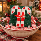 A square quilted fabric ornament or pillow with a candy cane design, placed in a decorative bowl filled with wrapped candy, evergreen branches, and red berries on a wooden table.