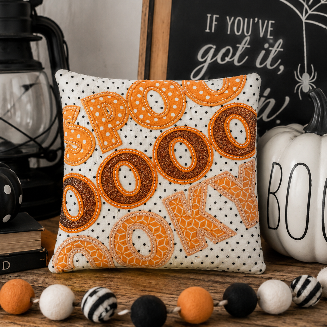 Decorative pillow with spider and web design in a bowl with Halloween-themed items.