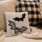 Decorative pillow with bat designs on a couch with plaid pillows and a candle.