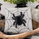 Decorative pillow with spider and web design in a bowl with Halloween-themed items.