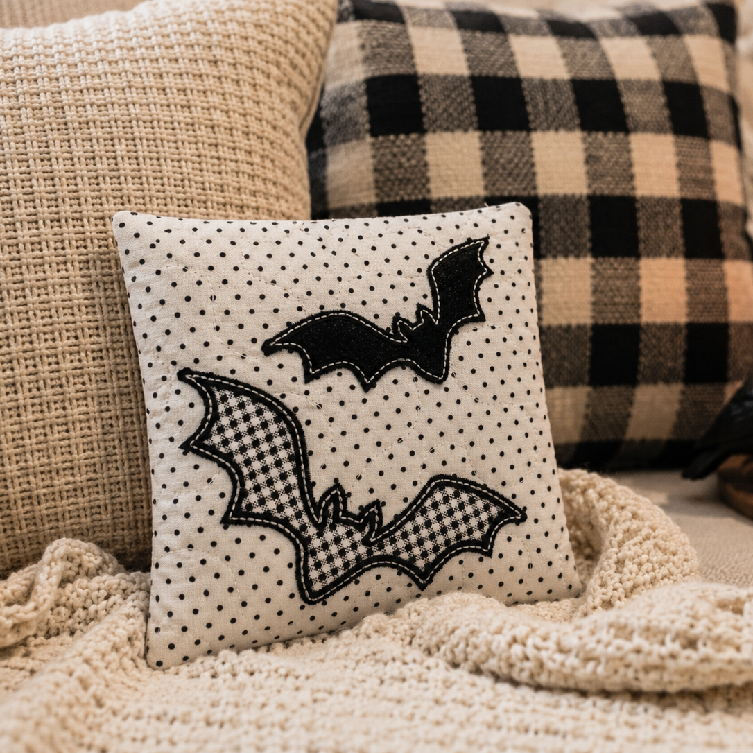 Decorative pillow with bat designs on a couch with plaid pillows and a candle.