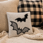 Decorative pillow with bat designs on a couch with plaid pillows and a candle.