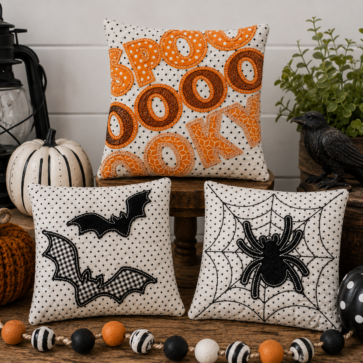 Three decorative square throw pillows styled in a fall Halloween setting. The top pillow features orange and brown polka-dot donuts spelling 'BOO' on a white background with black dots.