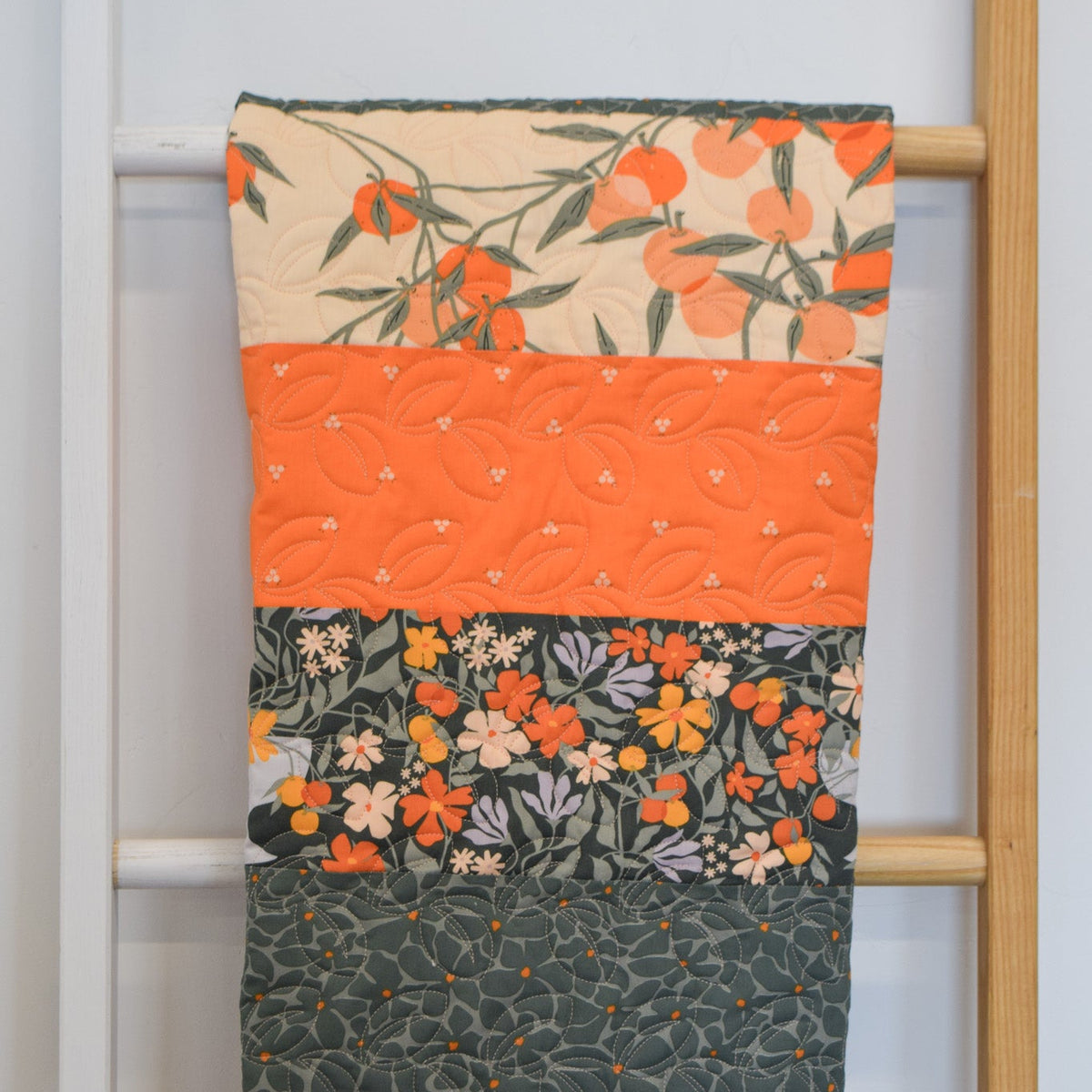 Floral-patterned quilt draped over a wooden ladder against a white wall