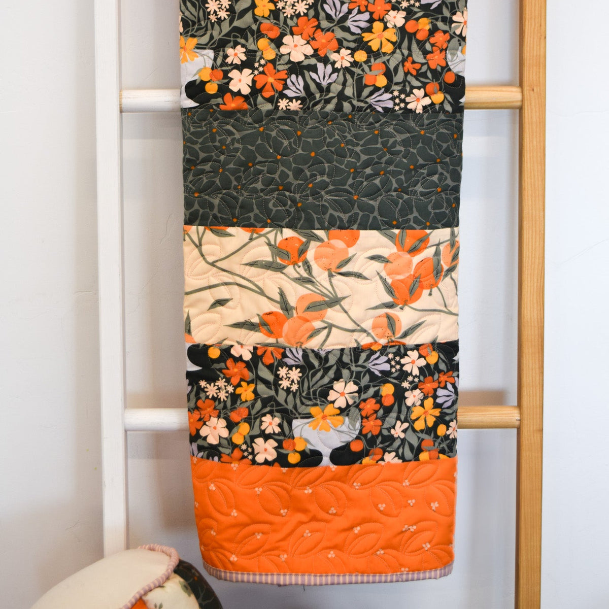 Floral-patterned quilt draped over a wooden ladder against a white wall.