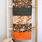 Floral-patterned quilt draped over a wooden ladder against a white wall.
