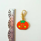 Pumpkin-shaped keychain with a smiley face next to a ruler on a white background