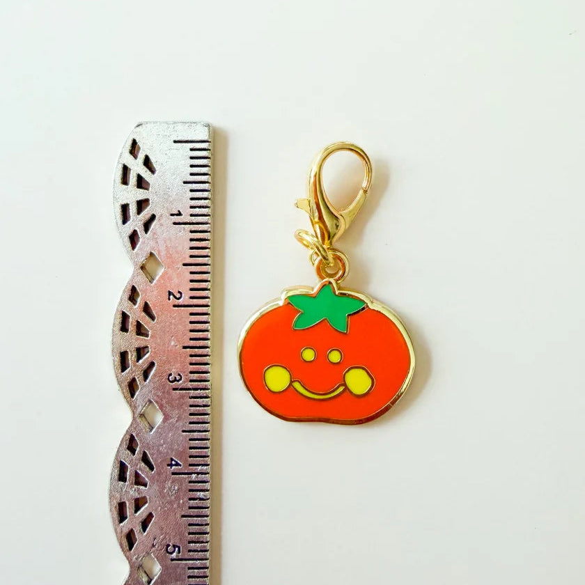 Pumpkin-shaped keychain with a smiley face next to a ruler on a white background