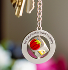 Keychain with 'My Girlfriend's Quilt Shoppe' logo and colorful design on a blurred background