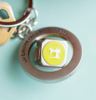 Keychain with a yellow circle and sewing machine design on a light blue background