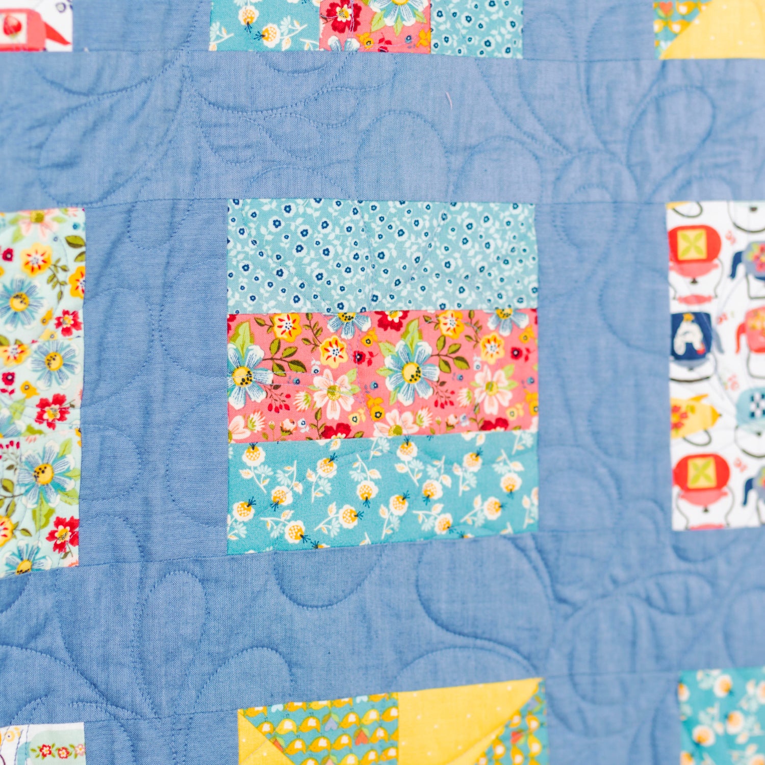 A close-up of a handmade quilted fabric panel with a blue background and colorful floral and patterned patchwork squares.