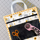 Fabric bag with sunflower design and zipper, containing scissors and a rotary cutter on a cutting mat.
