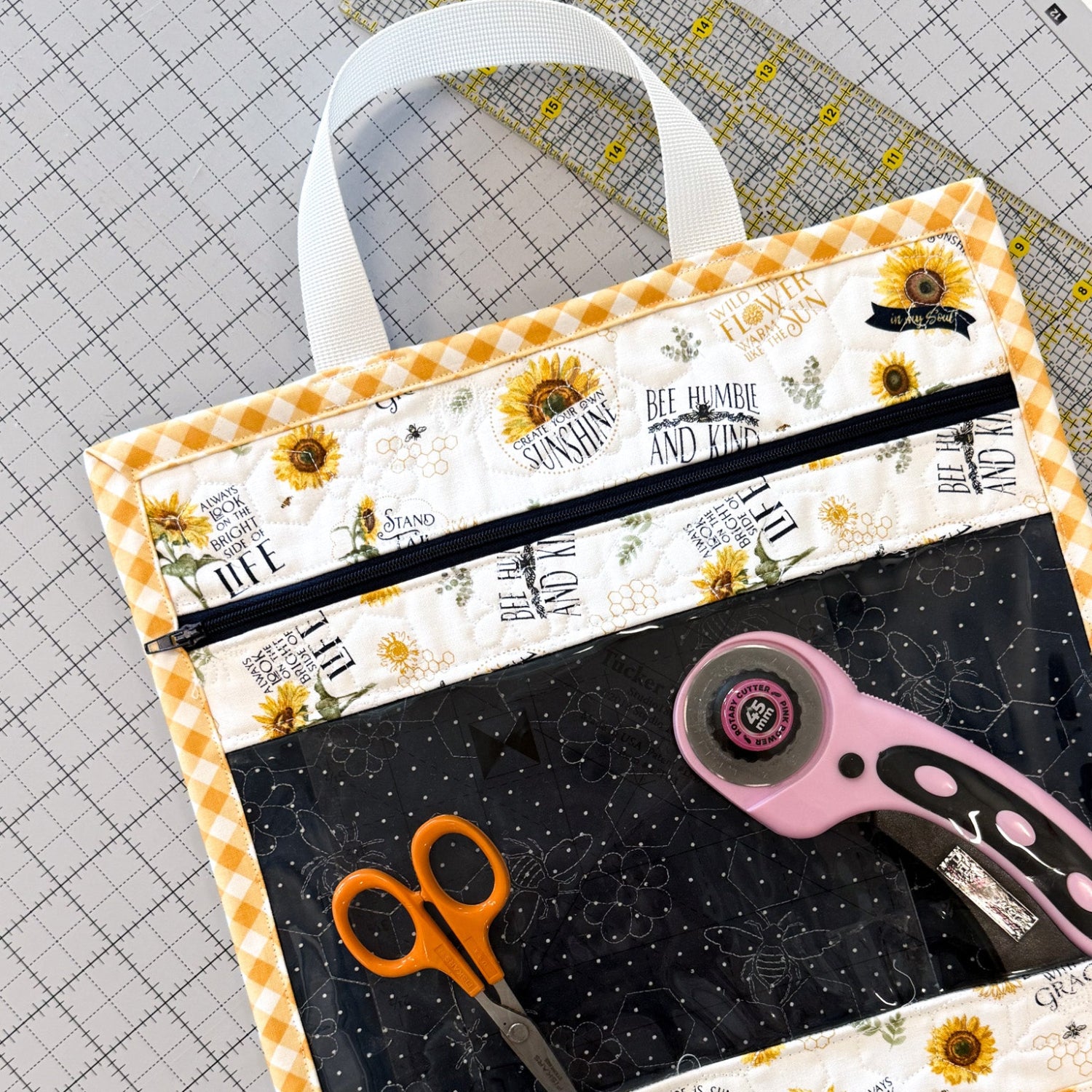 Fabric bag with sunflower design and zipper, containing scissors and a rotary cutter on a cutting mat.