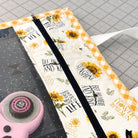 Fabric pouch with sunflower design and text on a cutting mat with scissors.