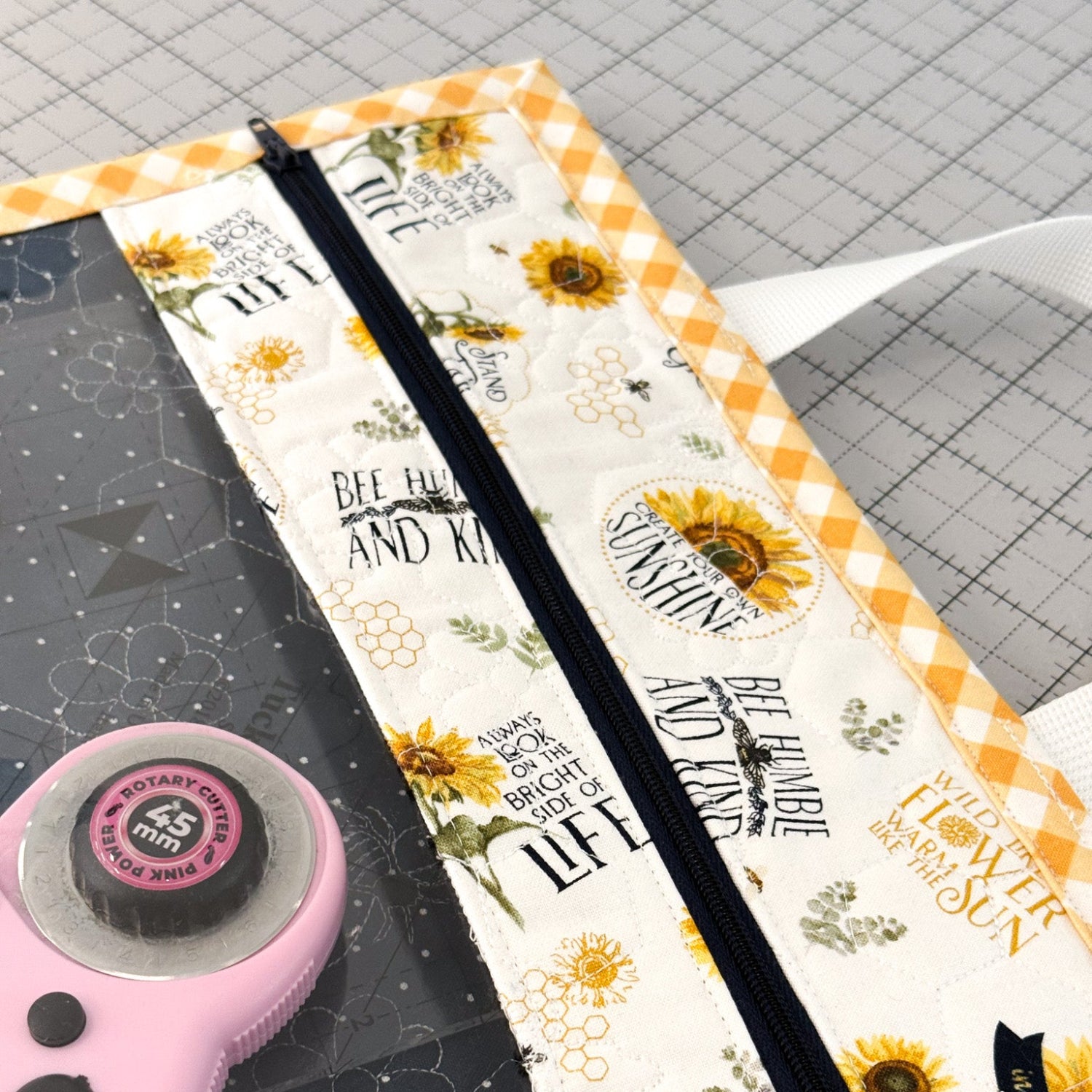 Fabric pouch with sunflower design and text on a cutting mat with scissors.