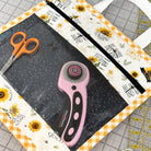 Crafting tools including a rotary cutter and scissors on a cutting mat with sunflower design.