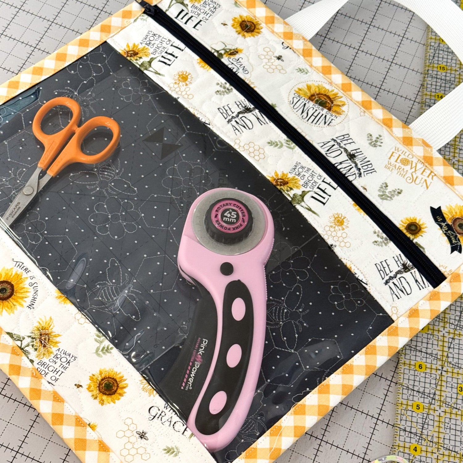 Crafting tools including a rotary cutter and scissors on a cutting mat with sunflower design.