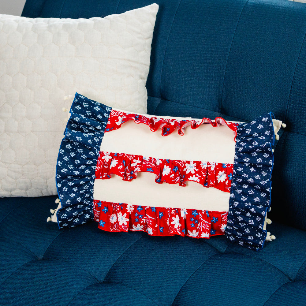 Three pillows on a blue couch: white, red, white, and blue pillow with floral patterns.