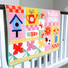 Colorful quilt with spring-themed designs hanging on a crib rail.