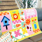 Colorful quilt with floral and nature-themed patterns draped over a sofa.